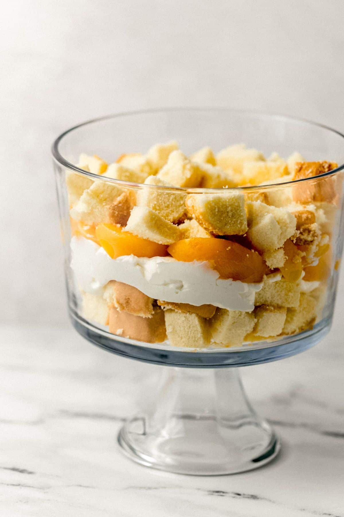 close up side view of layers of trifle being assembled in glass trifle bowl