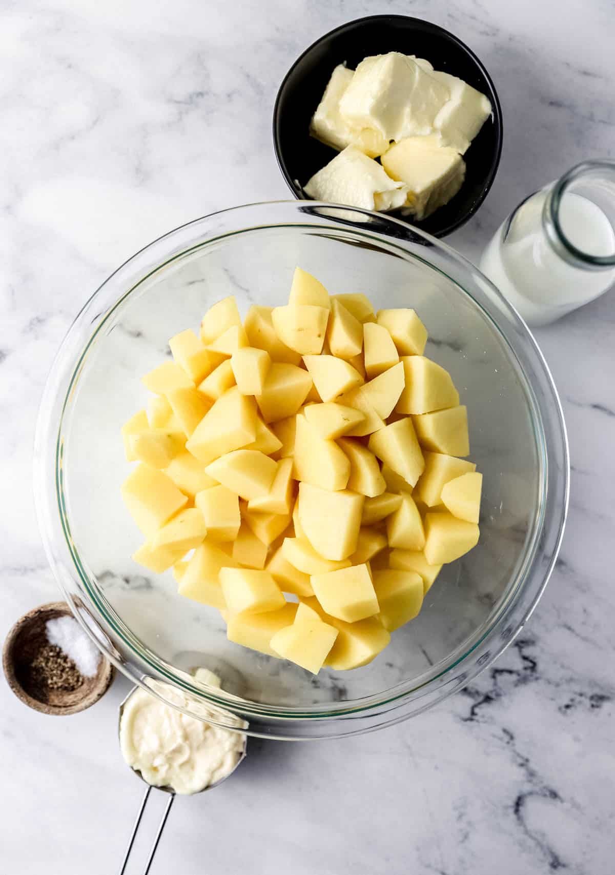 Ingredients needed to make mashed potaotes in separate bowls on marble surface. 