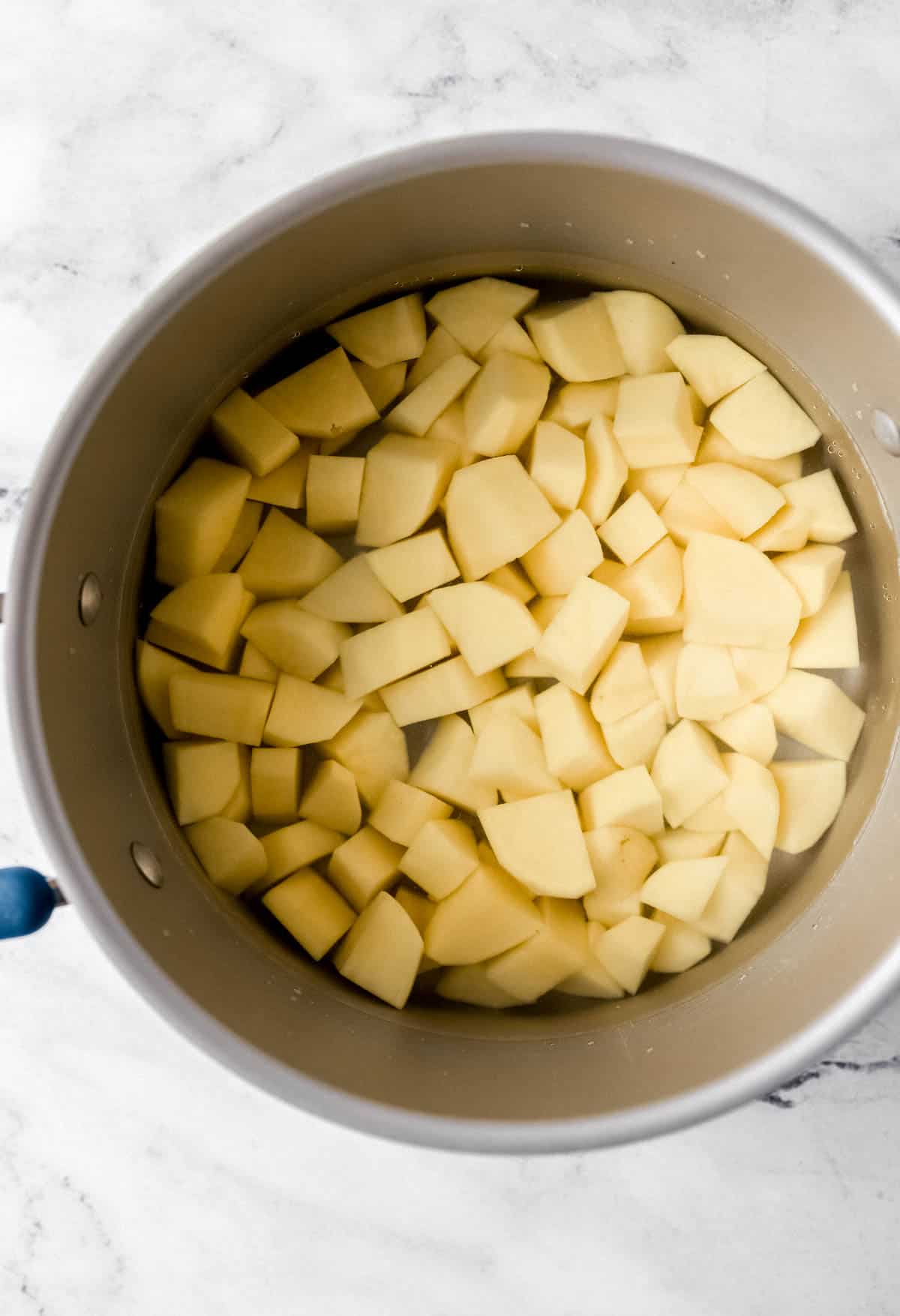 Overhead view of cut up potatoes in pot with water. 
