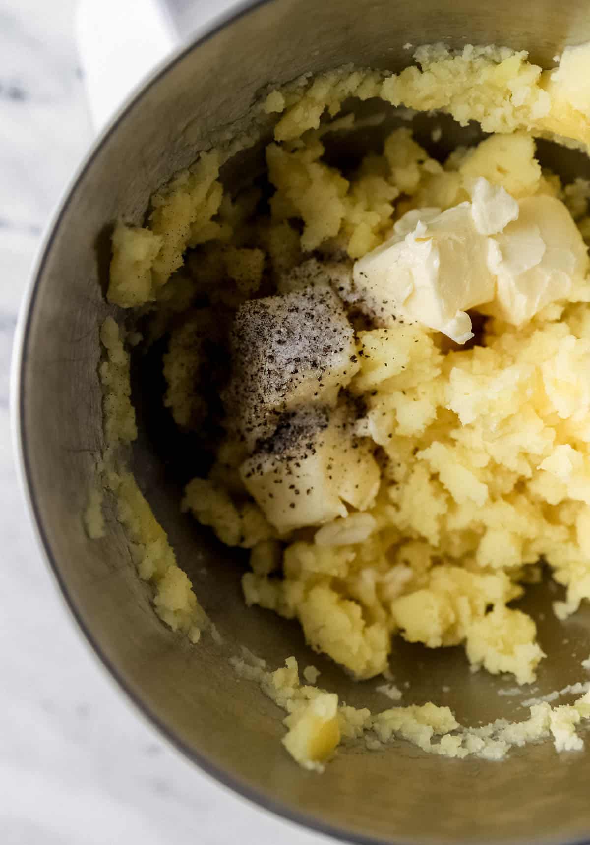 Butter, milk, salt, and pepper added to stand mixer bowl with potatoes. 