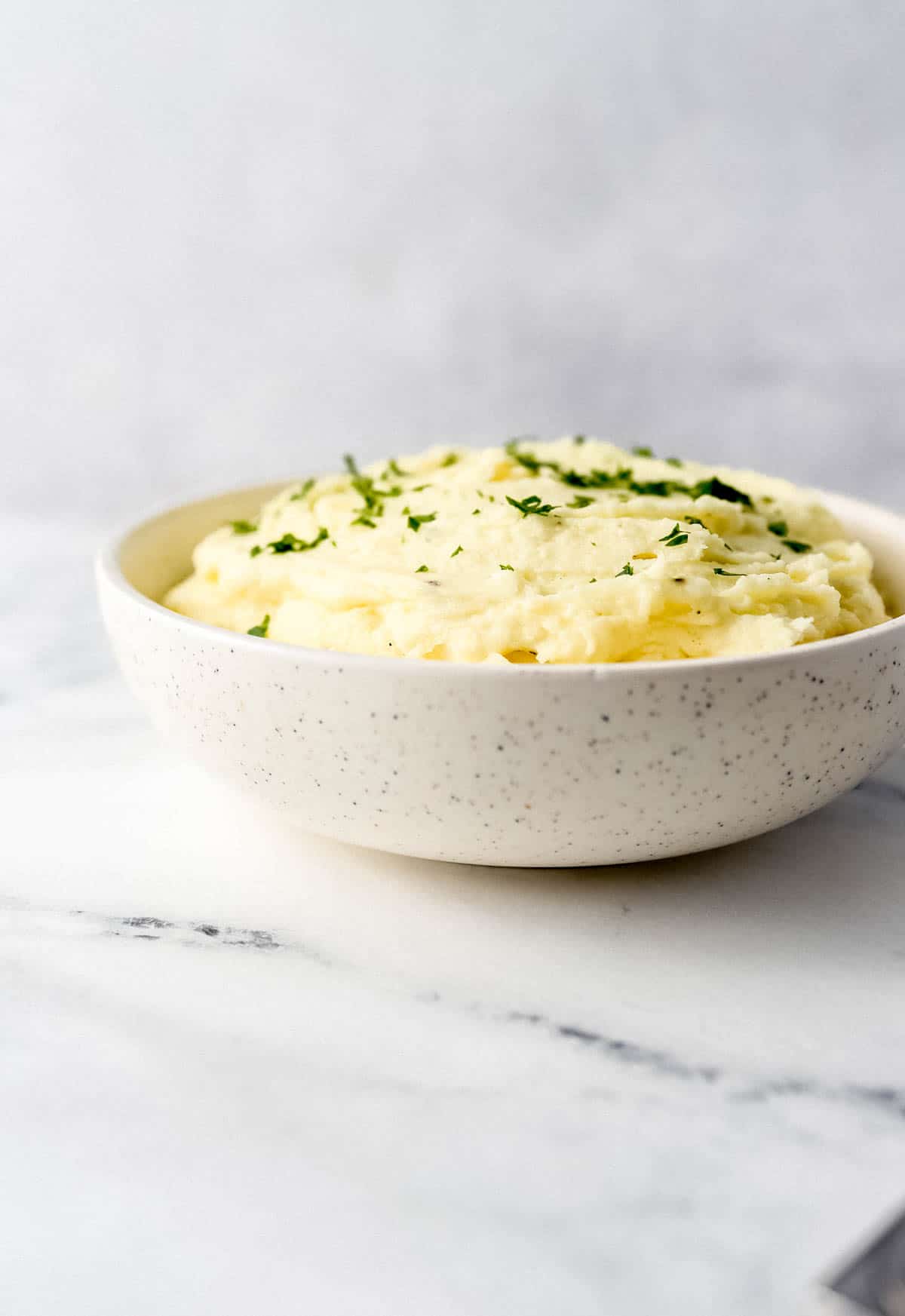 Close up side view of mashed potatoes in bowl on marble surface. 