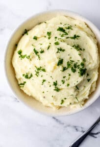 Mashed potatoes in bowl topped with parsley.