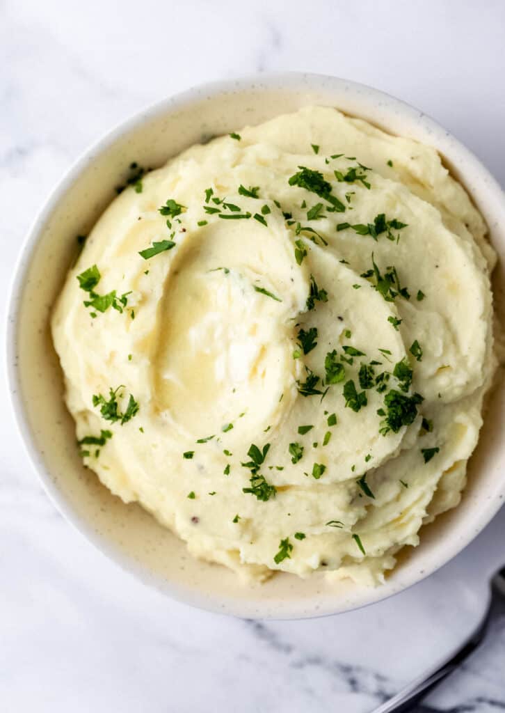 Overhead view of mashed potatoes in a white bowl topped with chopped parsley.