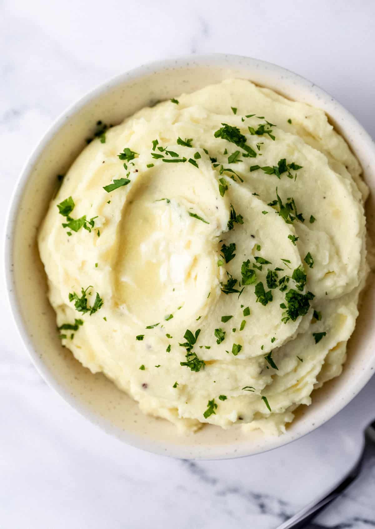 Overhead view of bowl of mashed potatoes topped with chopped fresh parsley. 