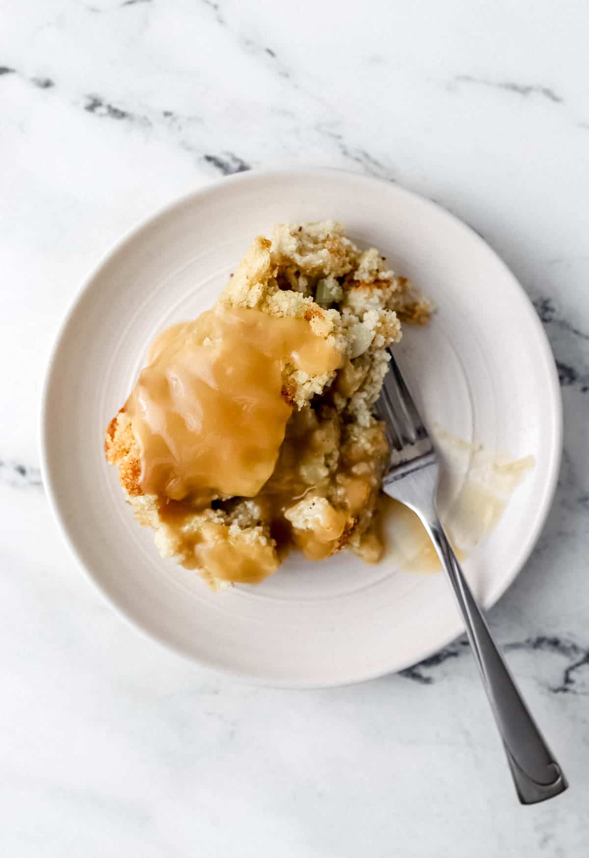 Single serving of cornbread dressing topped with gravy on a plate with a fork. 