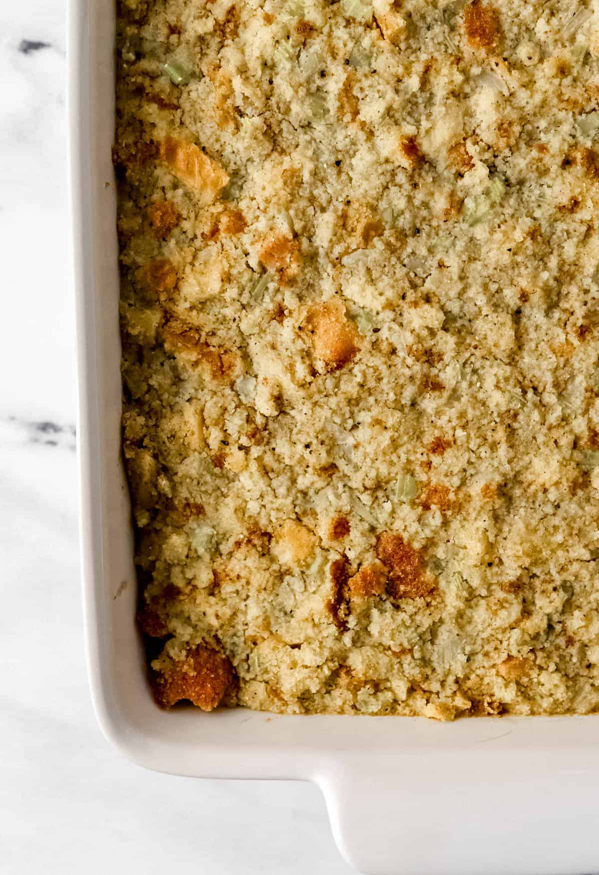 Overhead view of finished cornbread dressing in white baking dish on marble surface. 