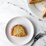 Overhead view of slice of cake on a white plate with the rest of the cake in the background.