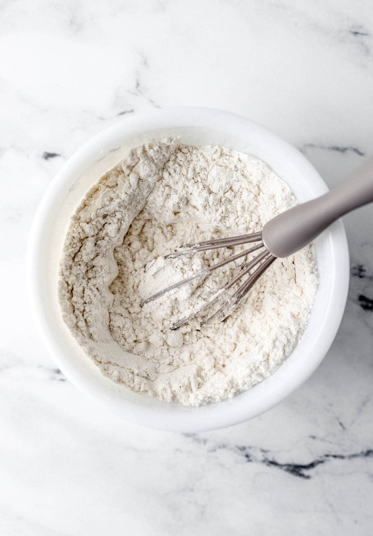 Dry ingredients in a white mixing bowl with a whisk.