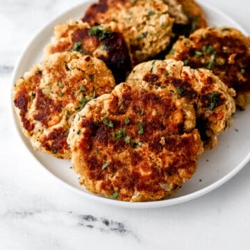 Close up view of finished salmon patties on white plate.