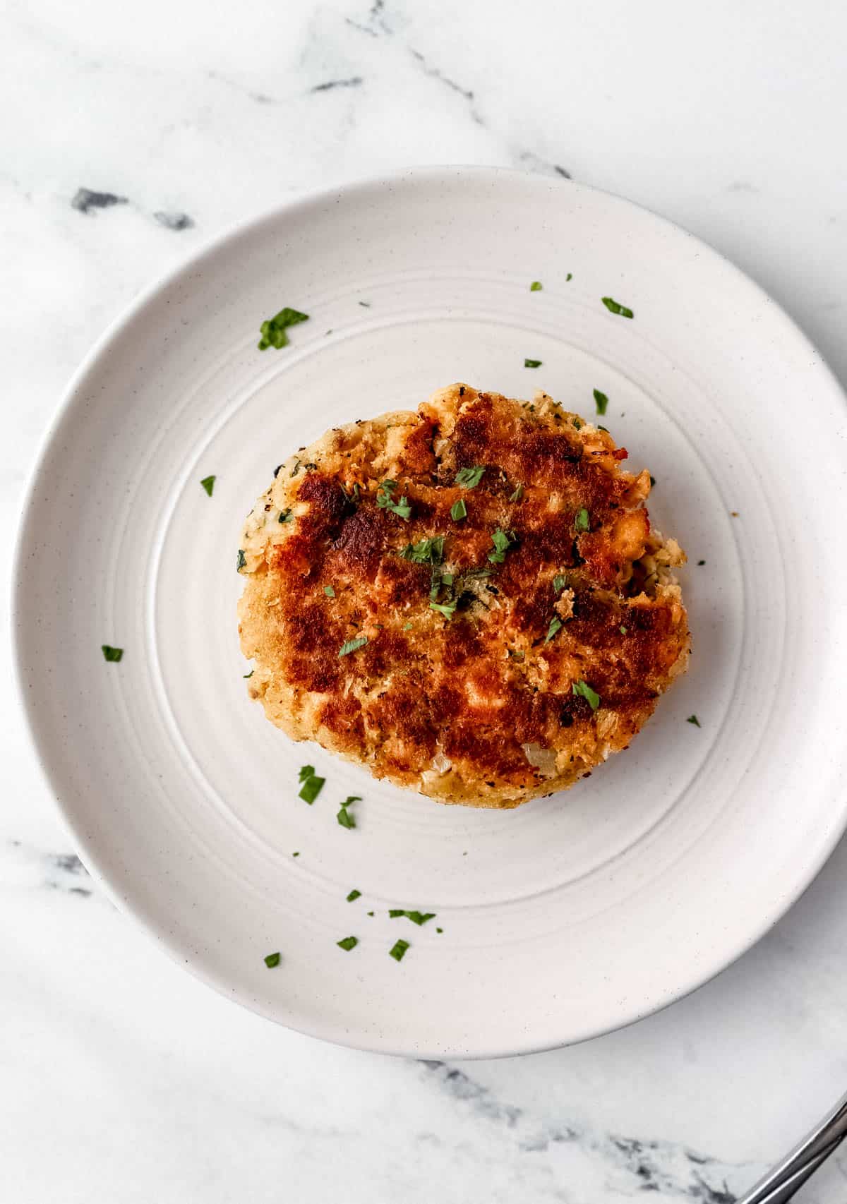 Overhead view of white plate with finished patty on it. 