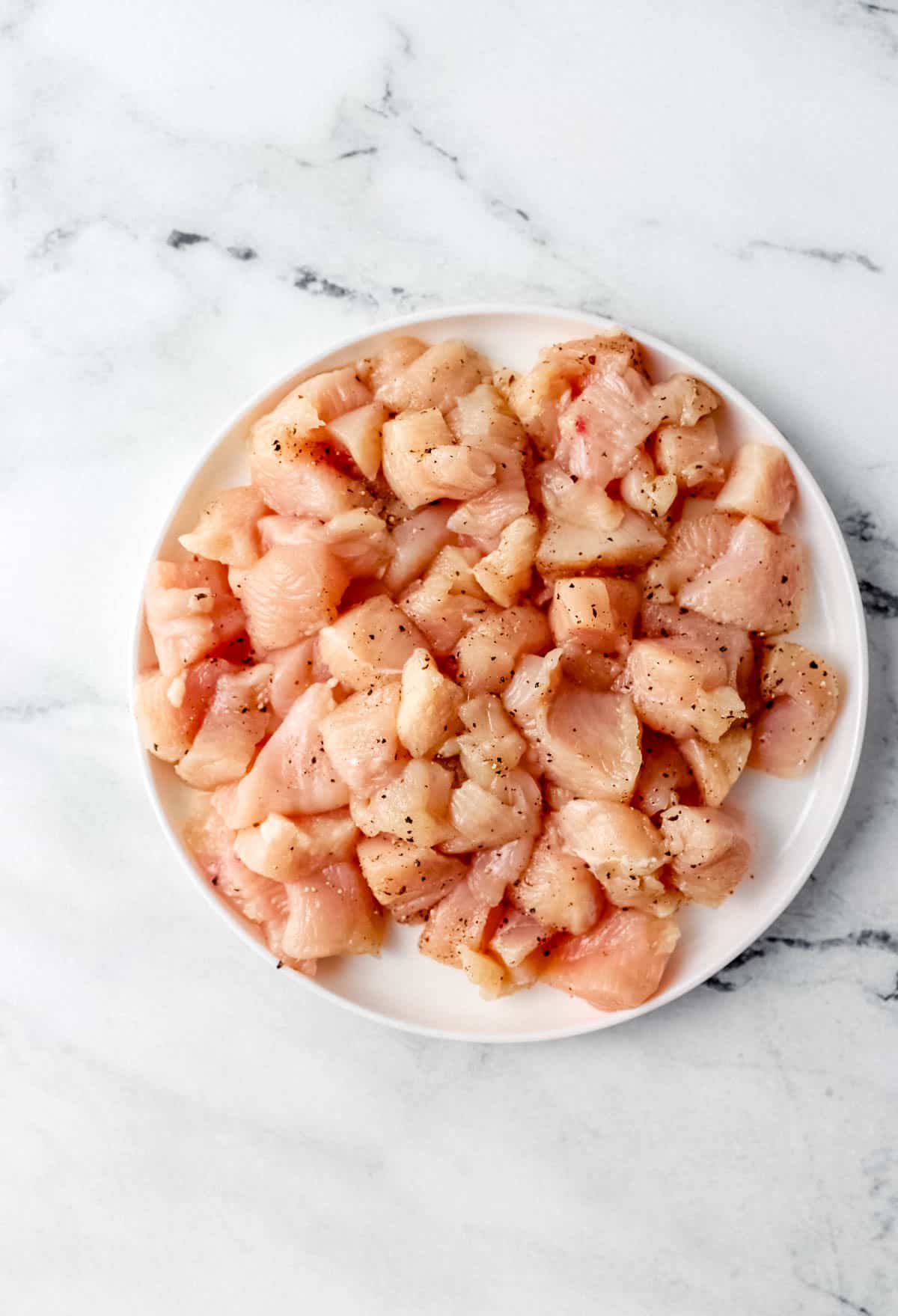 Cut up raw chicken that has been seasoned on white plate. 