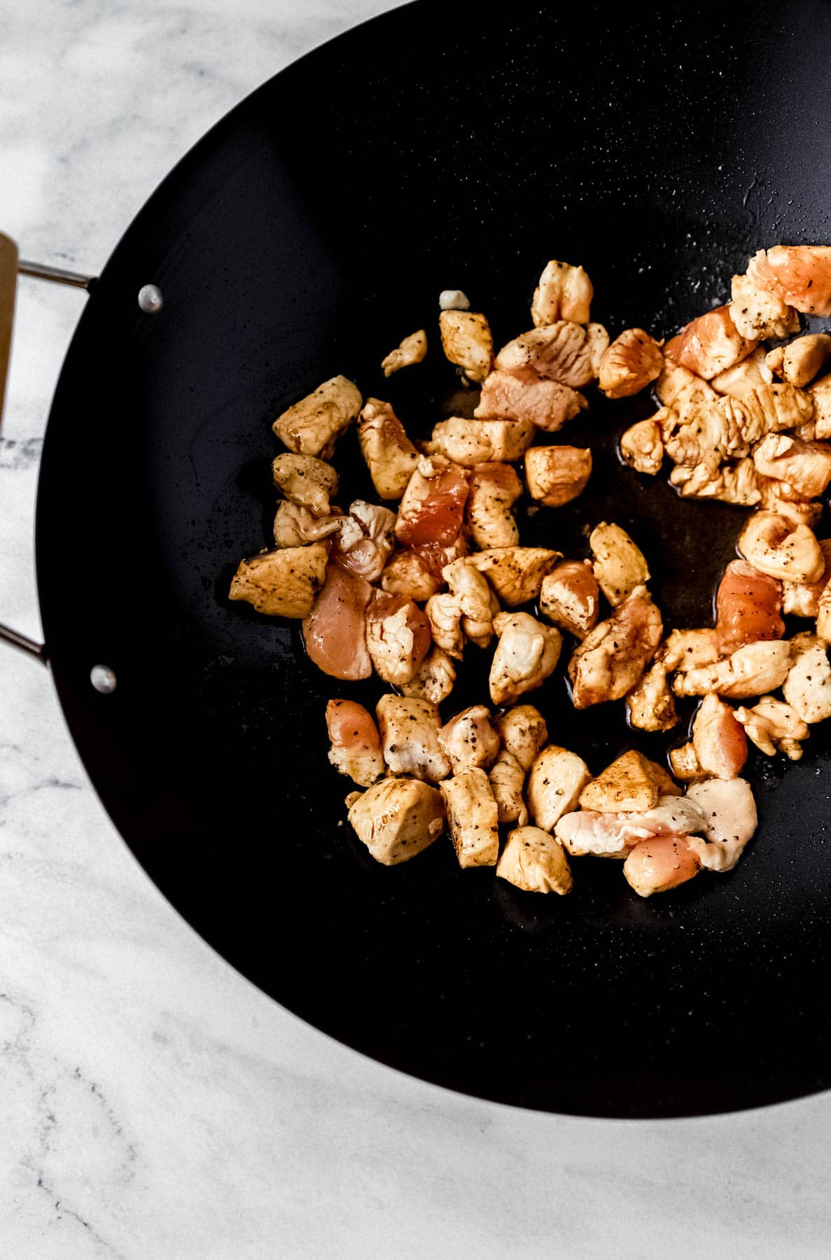 Chicken, oil, soy sauce added to wok on marble surface. 