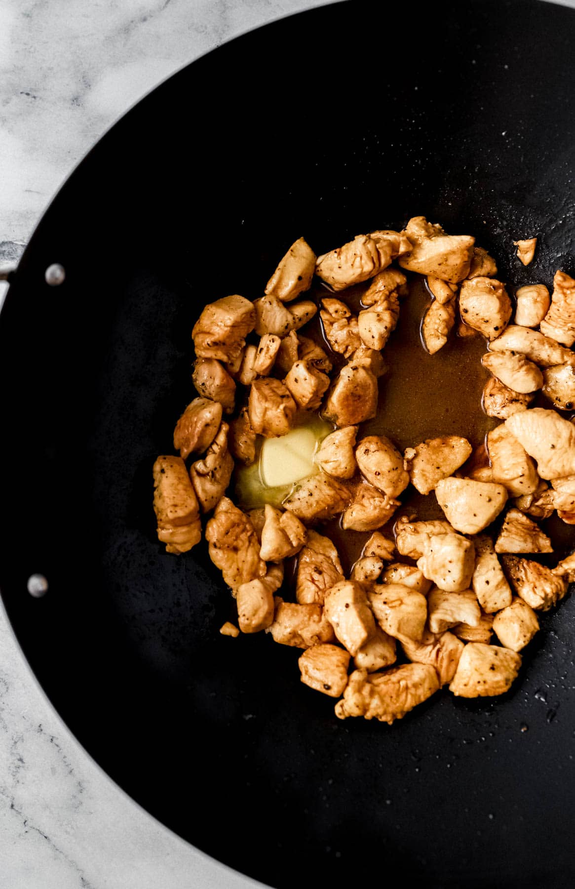 overhead view of butter added to chicken in wok 