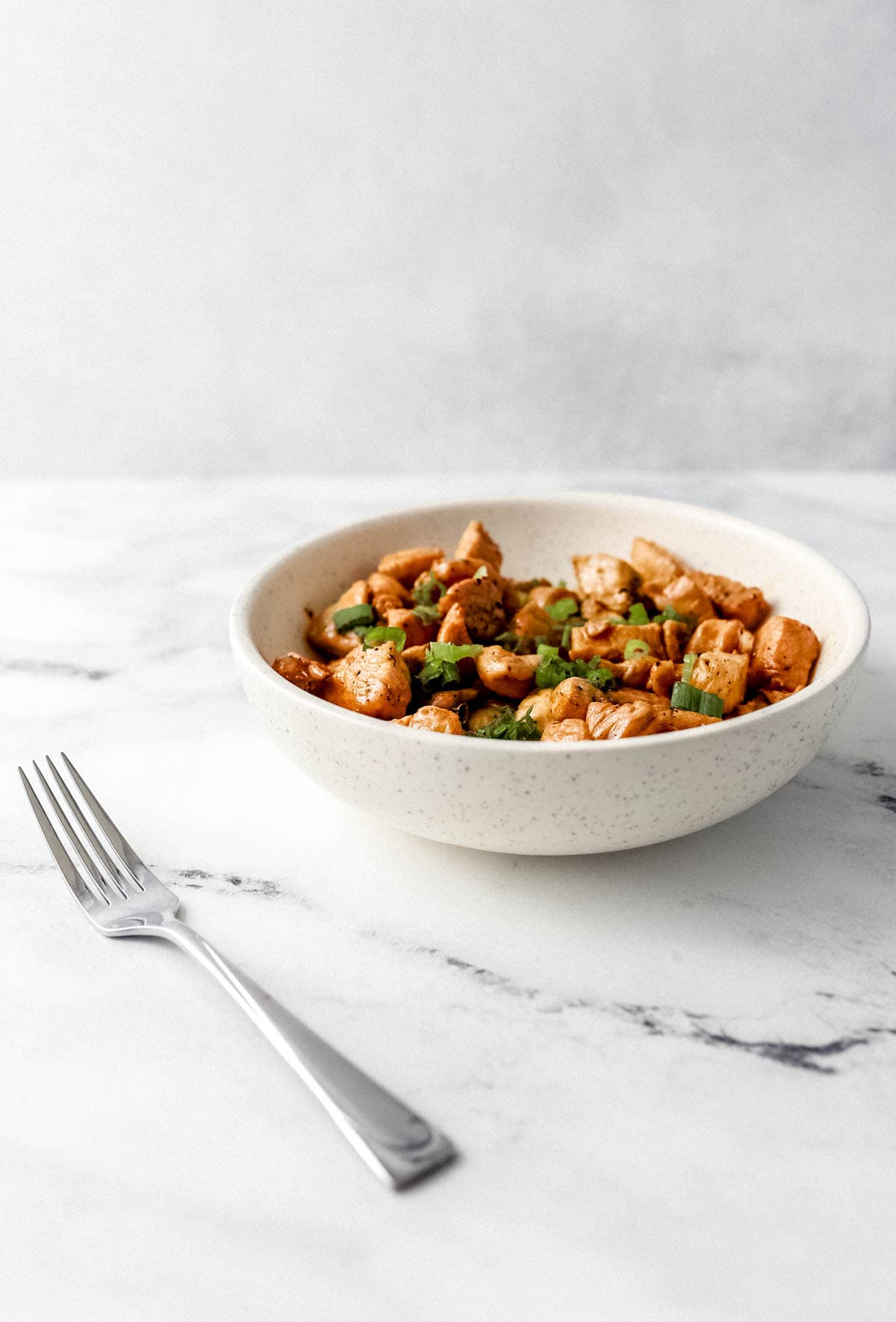 Close up side view of chicken in a bowl on marble surface by a fork. 