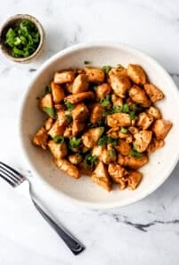 Finished chicken in bowl by fork and green onions.