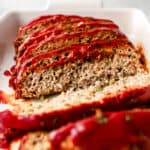 Close up view of finished and sliced meatloaf in white baking dish.