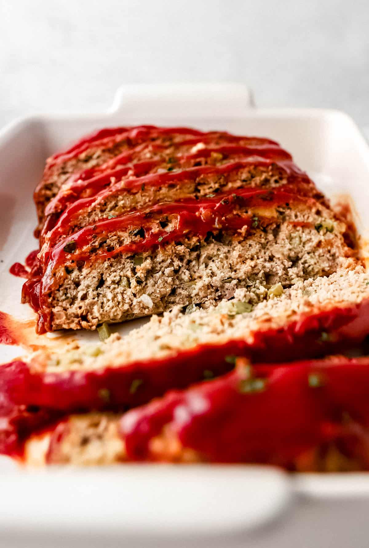 Close up side view of sliced meatloaf in baking dish. 