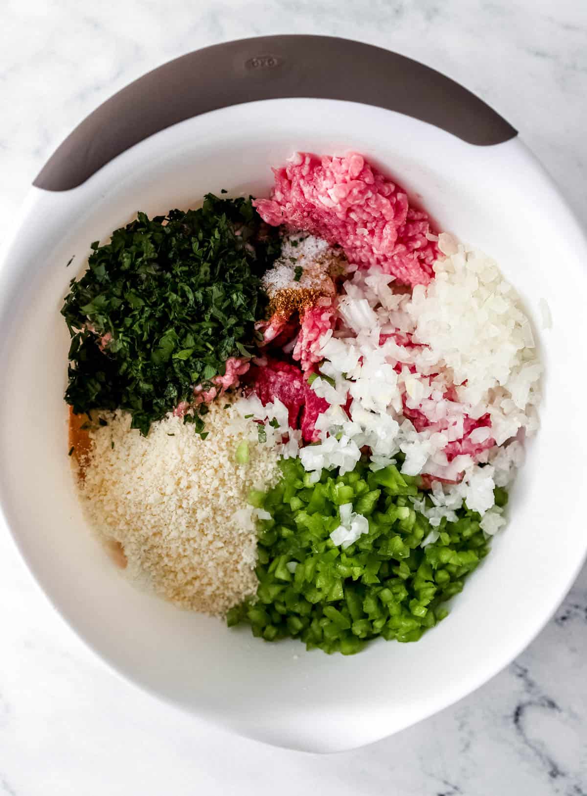 Overhead view of meatloaf ingredients added to large white bowl before combining. 