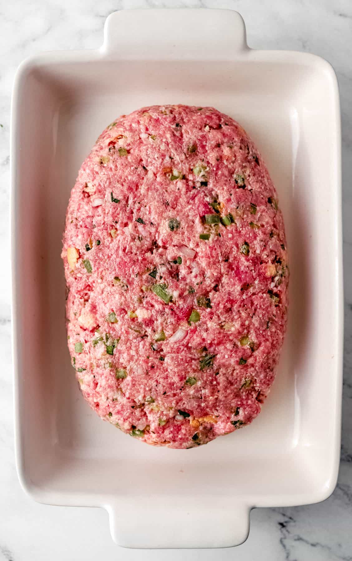 Meat mixture formed into loaf in a white rectangle baking dish. 