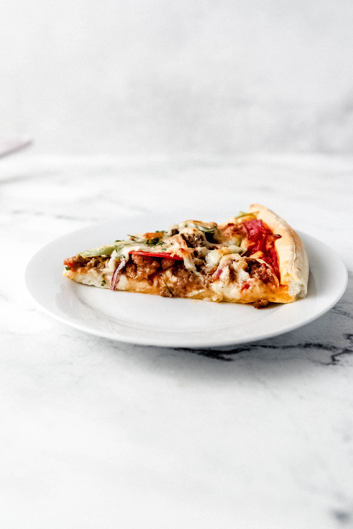 Close up side view of slice of pizza on a white plate. 