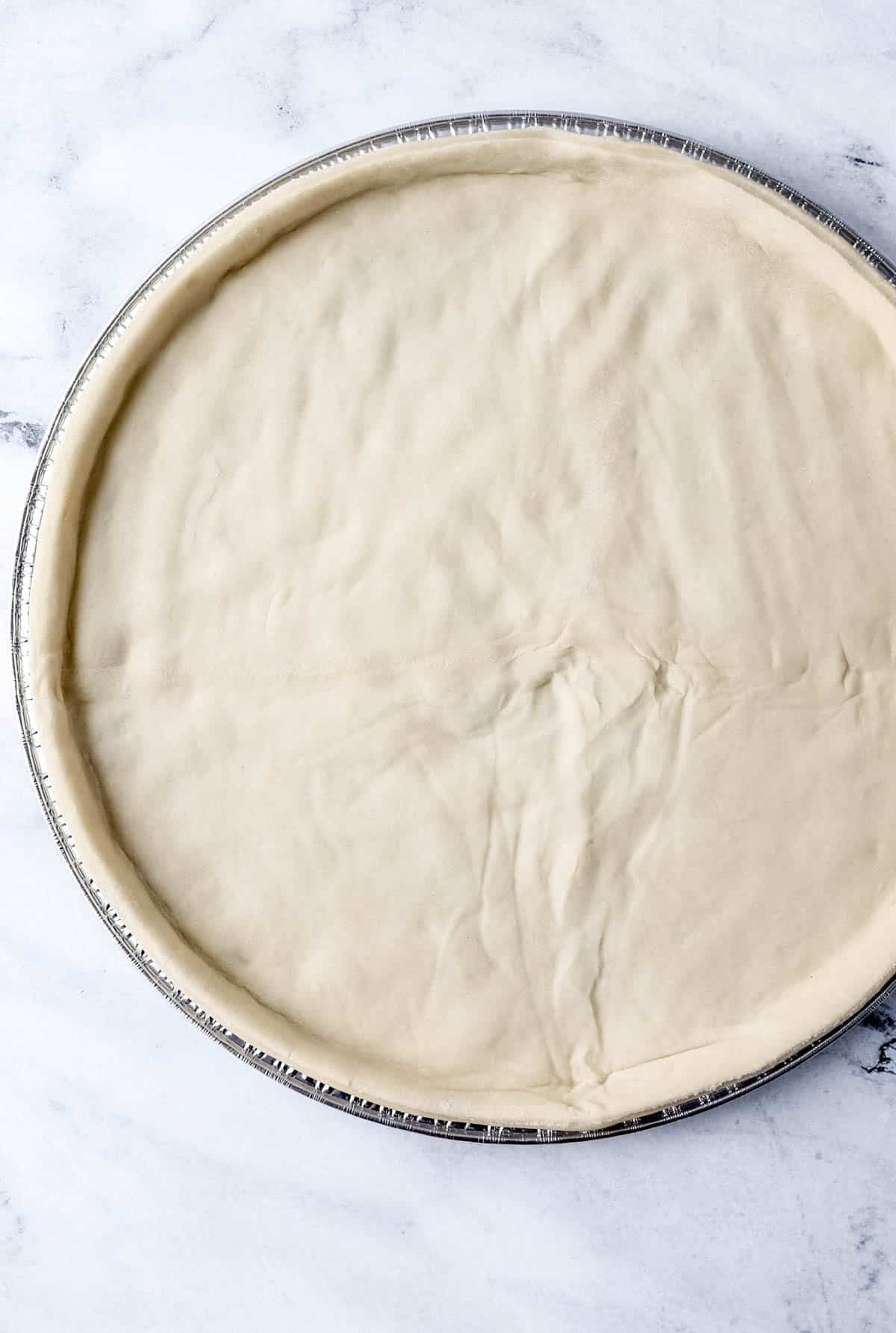 Pizza dough rolled out on a pizza pan. 