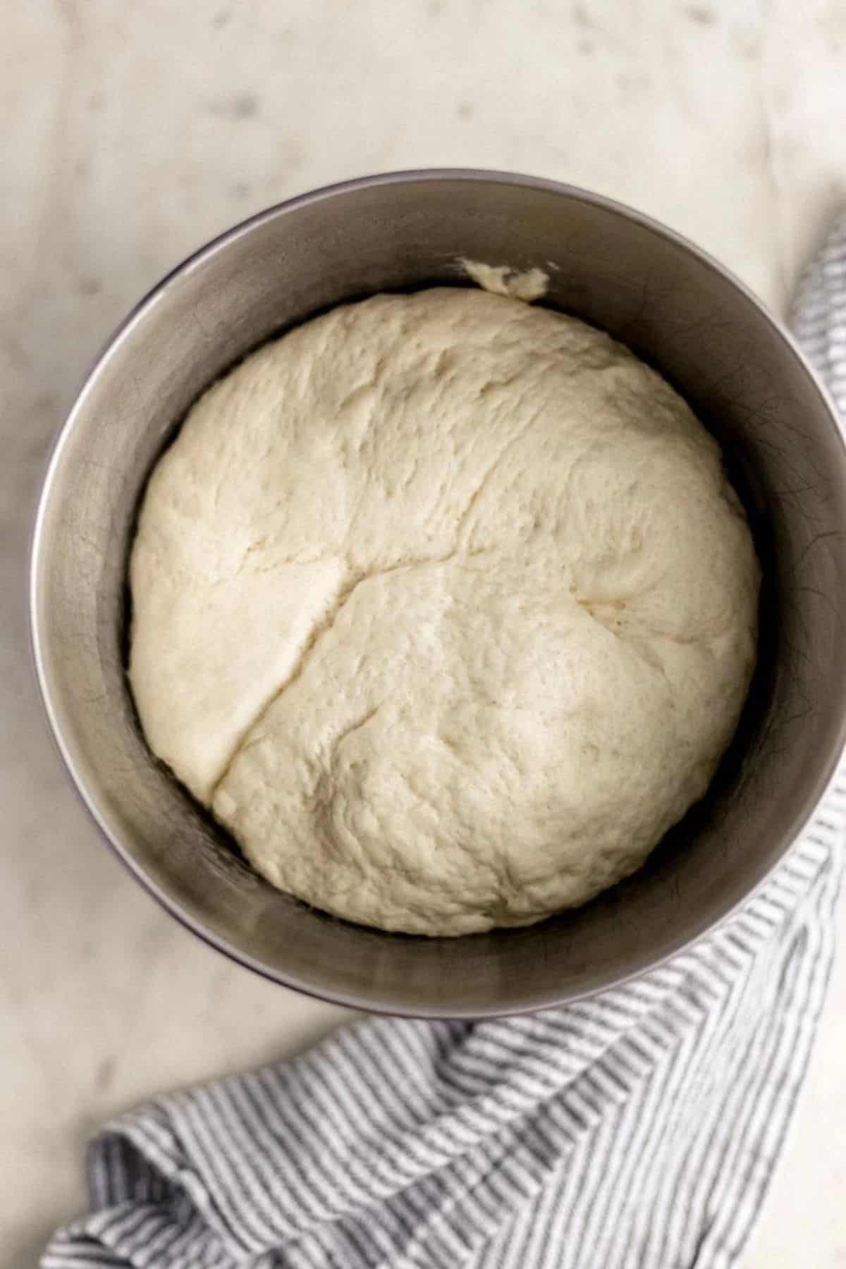 Pizza dough in stand mixer bowl beside a cloth napkin. 