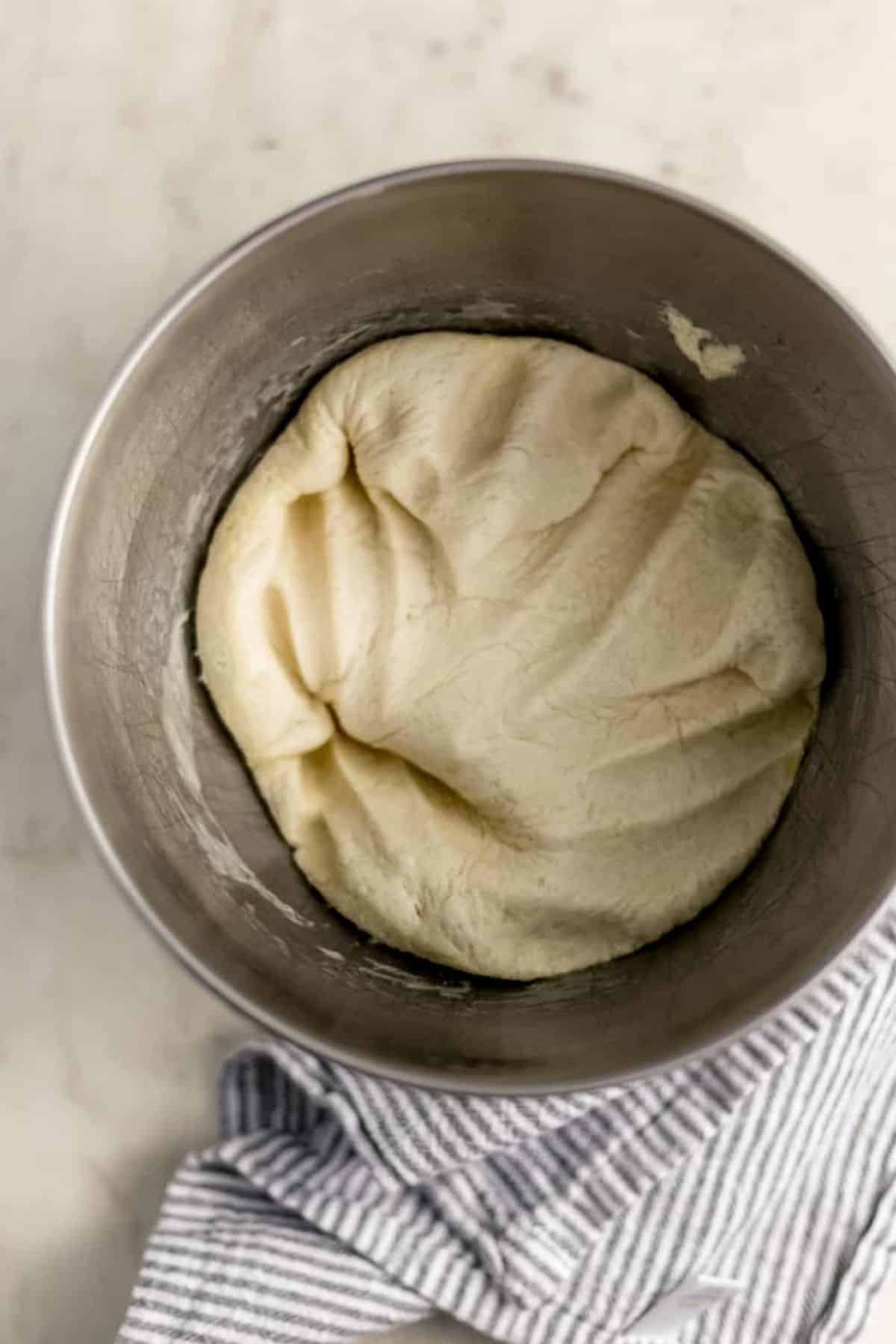 Air pressed out of pizza dough in stand mixer bowl beside a cloth napkin.