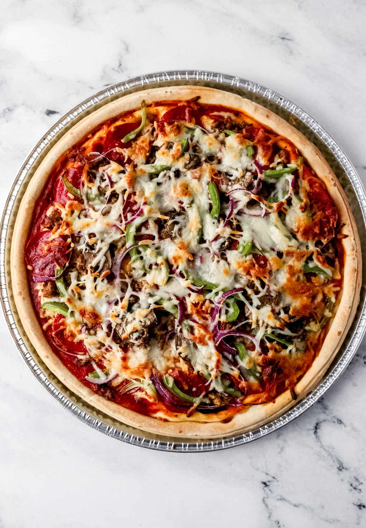 Overhead view of finished pizza in pan on marble surface. 