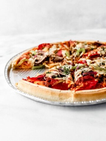Close up size view of finished whole pizza with a slice taken out of it.