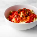 Close up side view of white bowl of chicken and pasta.