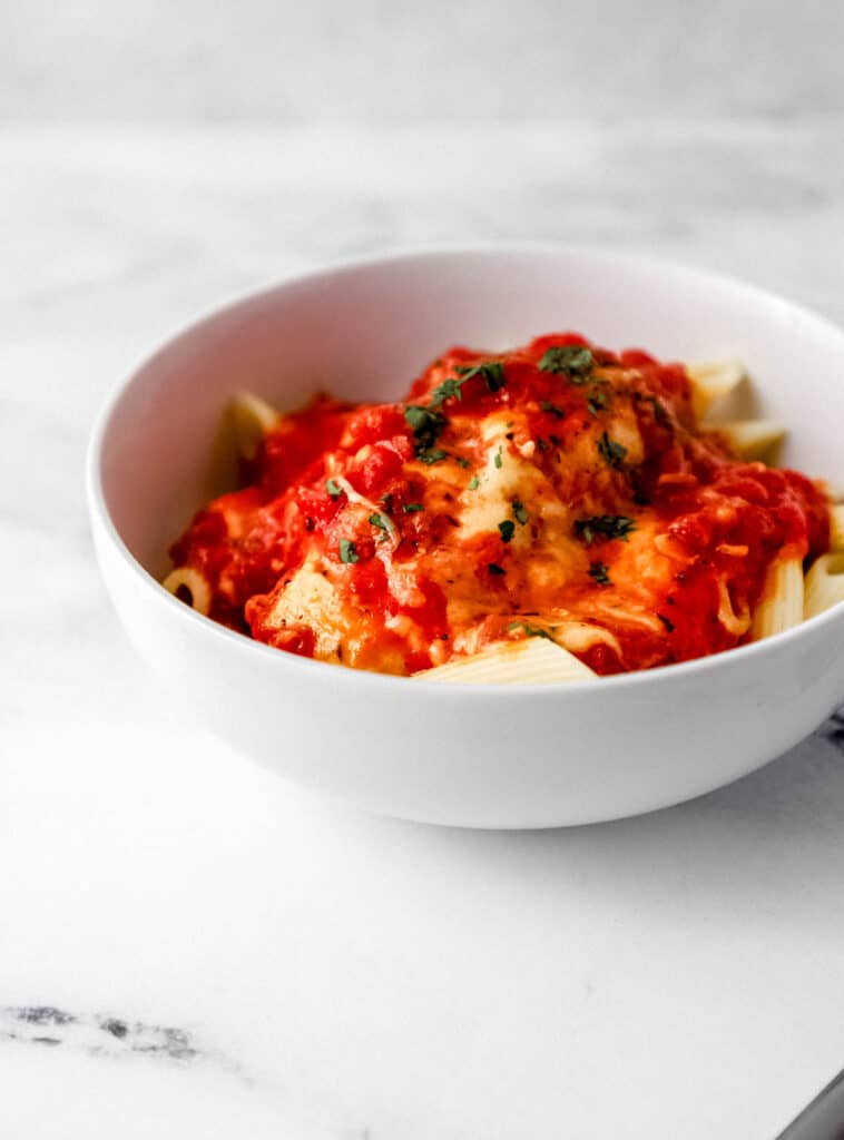 Close up side view of white bowl of chicken and pasta.