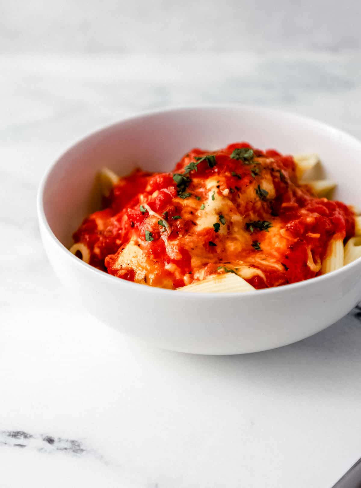 Close up side view of white bowl of chicken mozzarella over pasta. 