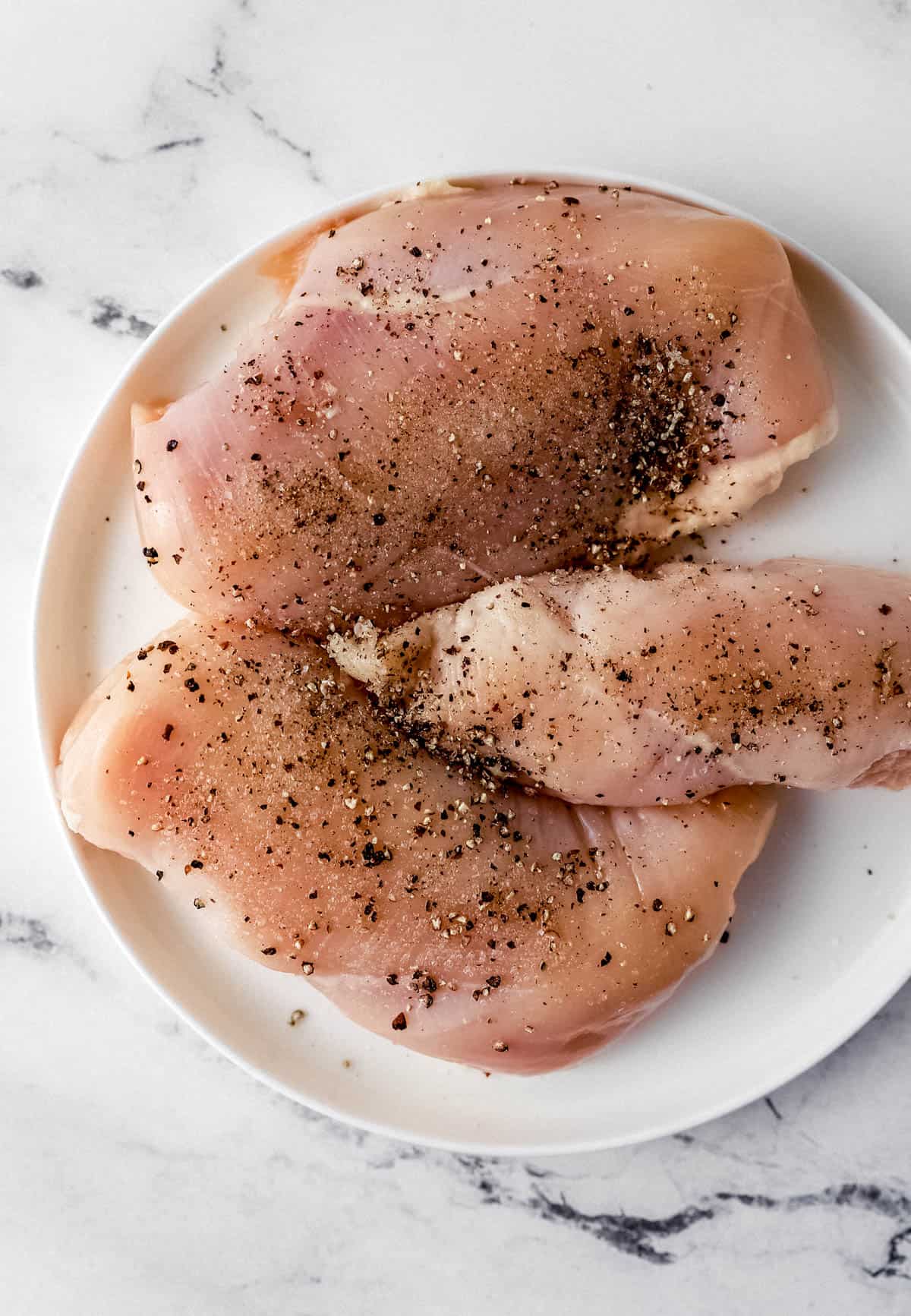 Raw seasoned chicken breasts on white plate 