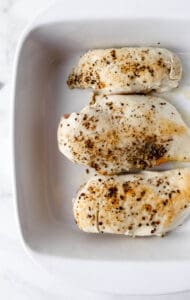 Cooked chicken breasts in a white baking dish.