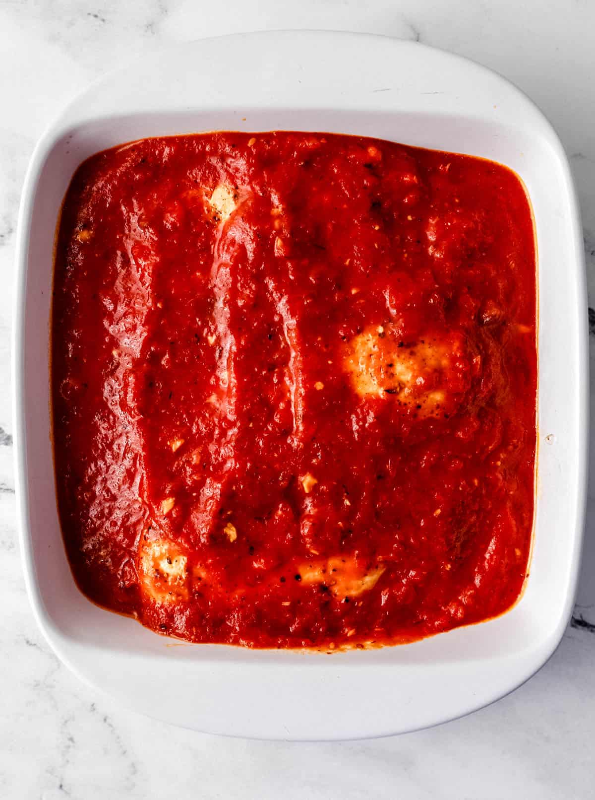 Overhead view of chicken topped with sauce in white baking dish. 