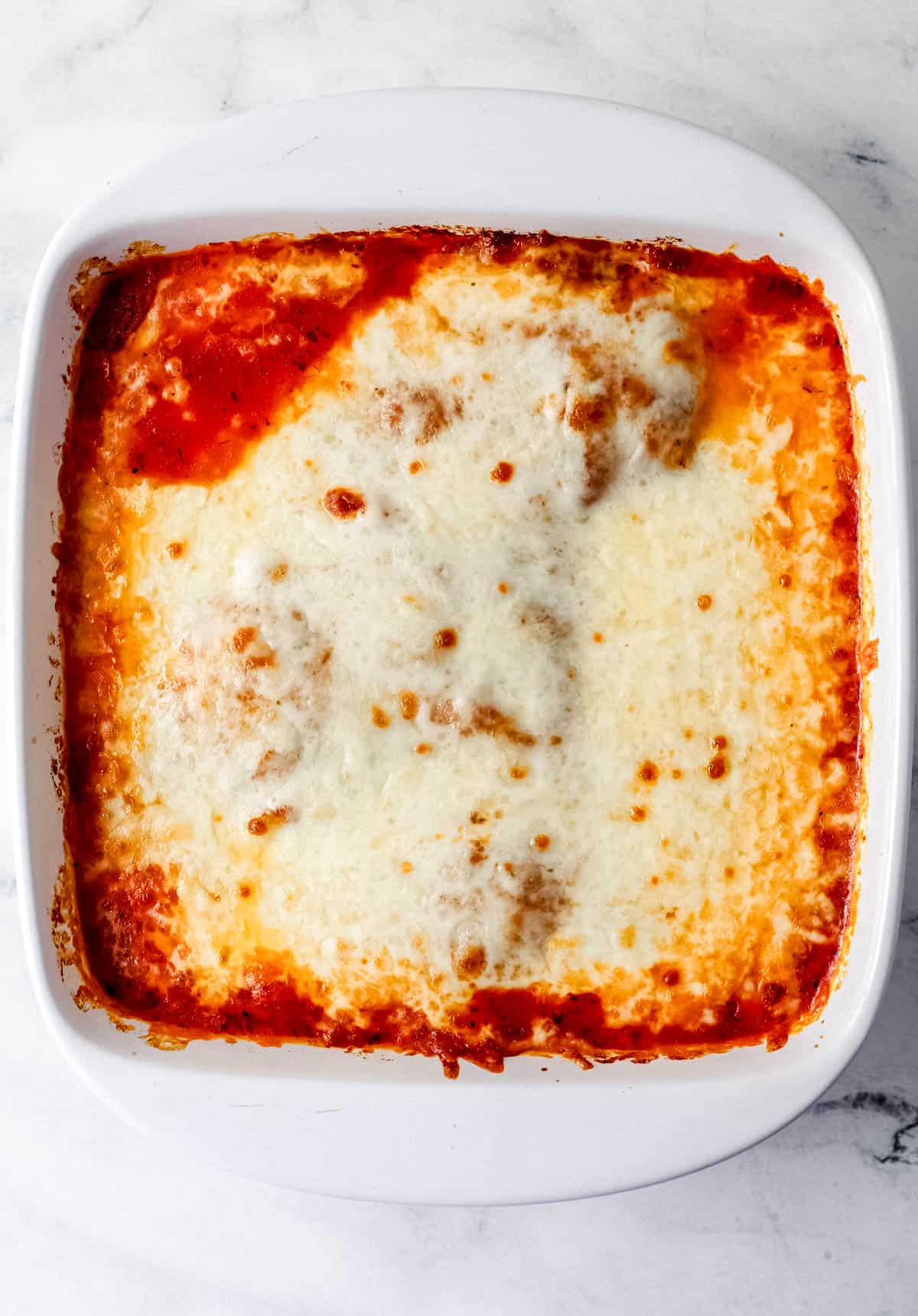 Overhead view of finished chicken mozzarella in white baking dish. 