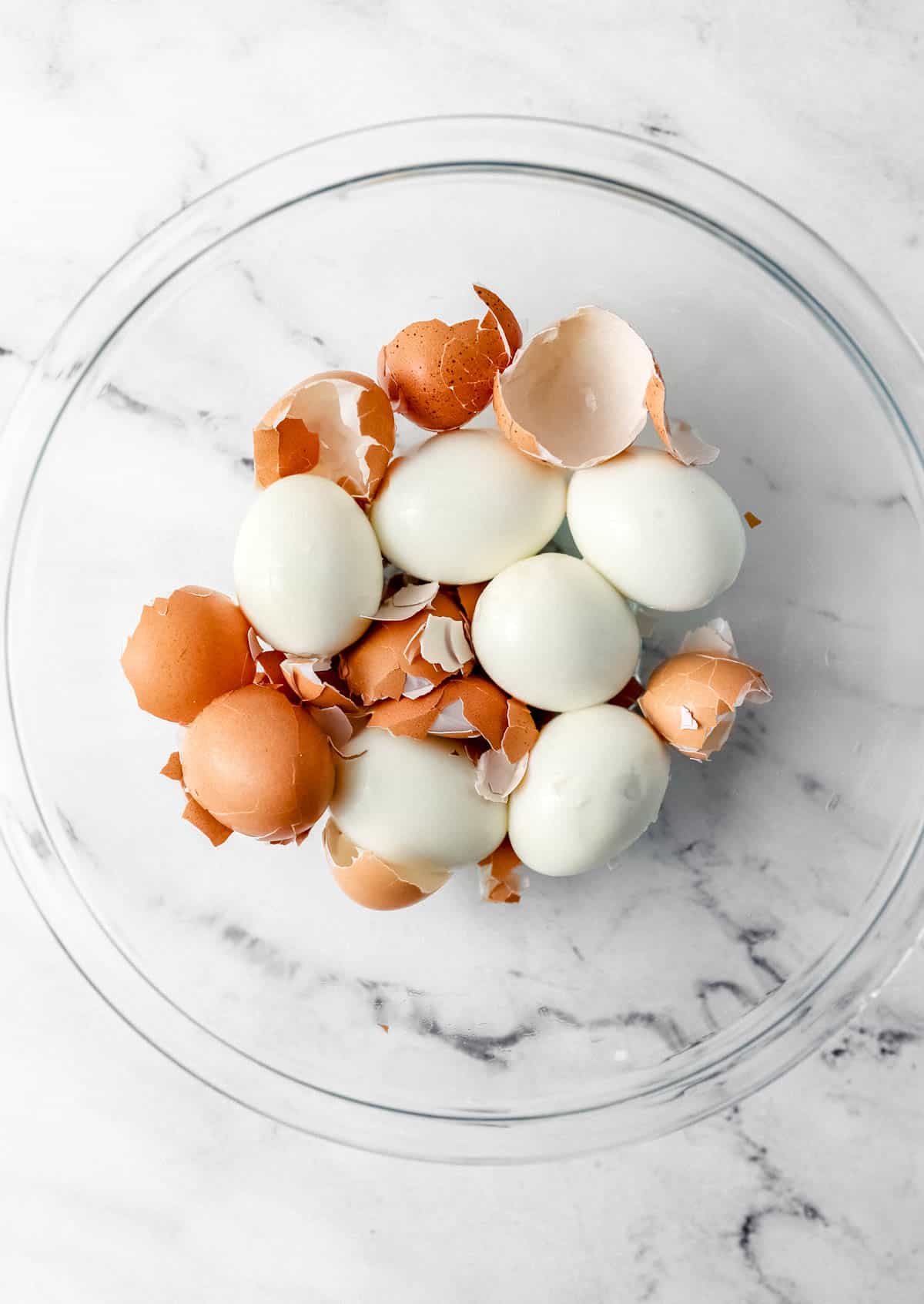 Large glass bowl with six hard boiled eggs, peeled with shells still in the bowl. 