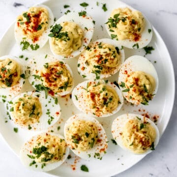 Overhead view of deviled eggs on a white plate topped with parsley and paprika.