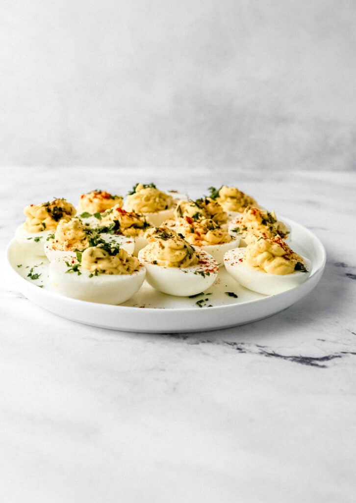 Close up side view of deviled eggs on white plate on marble surface.