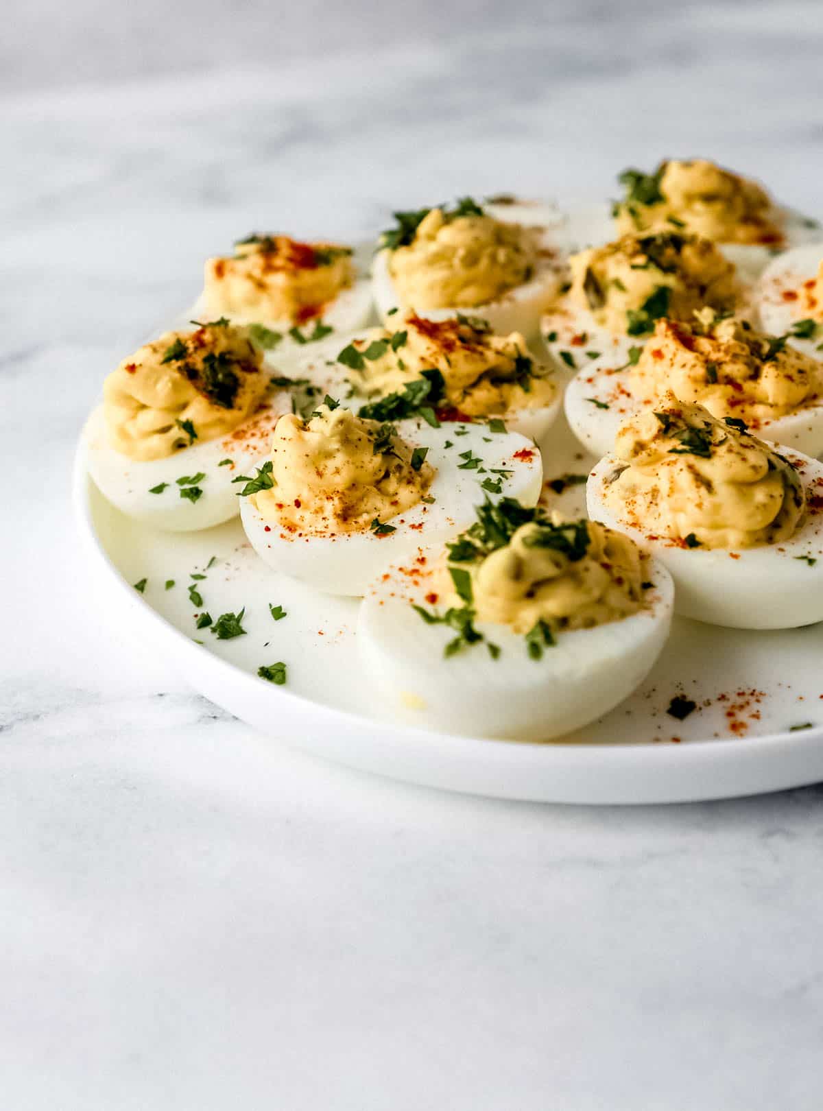 Close up side view of eggs on white plate topped with chopped parsley and paprika. 