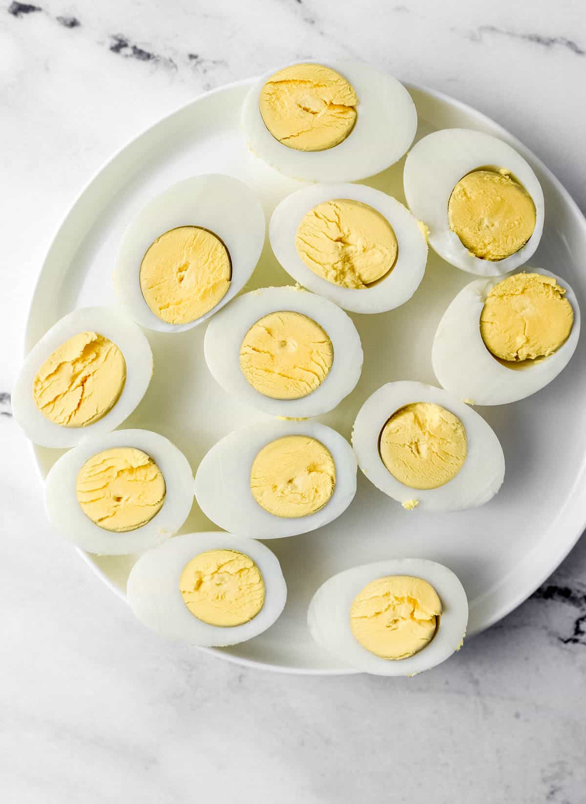 Hard boiled eggs cut in half on white plate. 