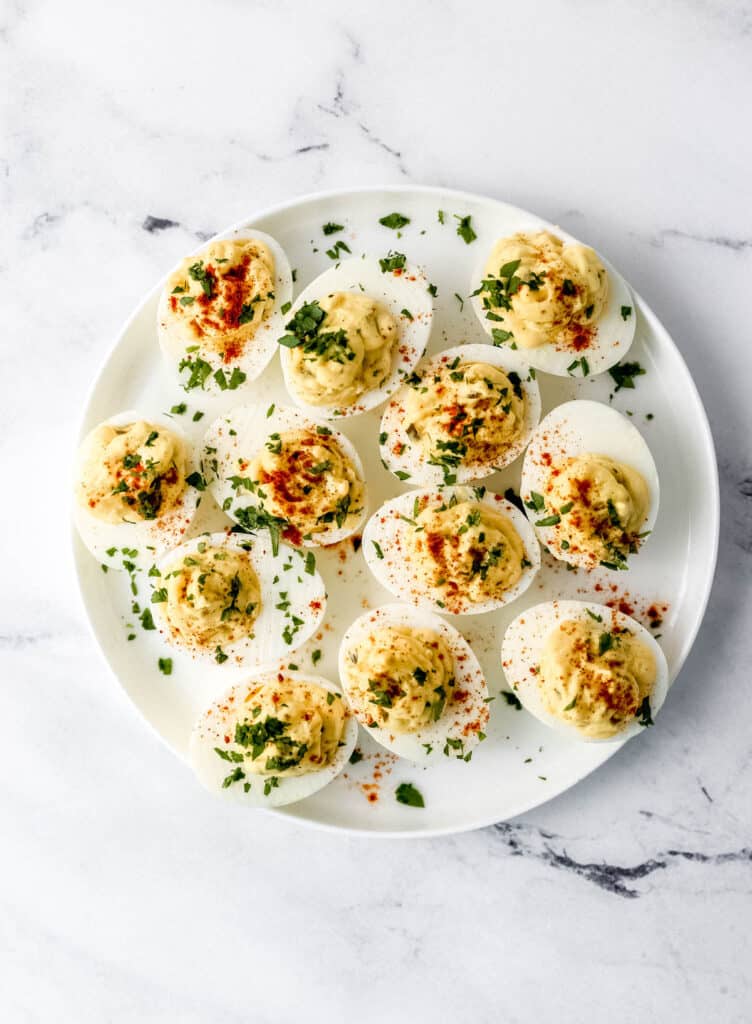 Deviled eggs on a white plate topped with parsley and paprika.