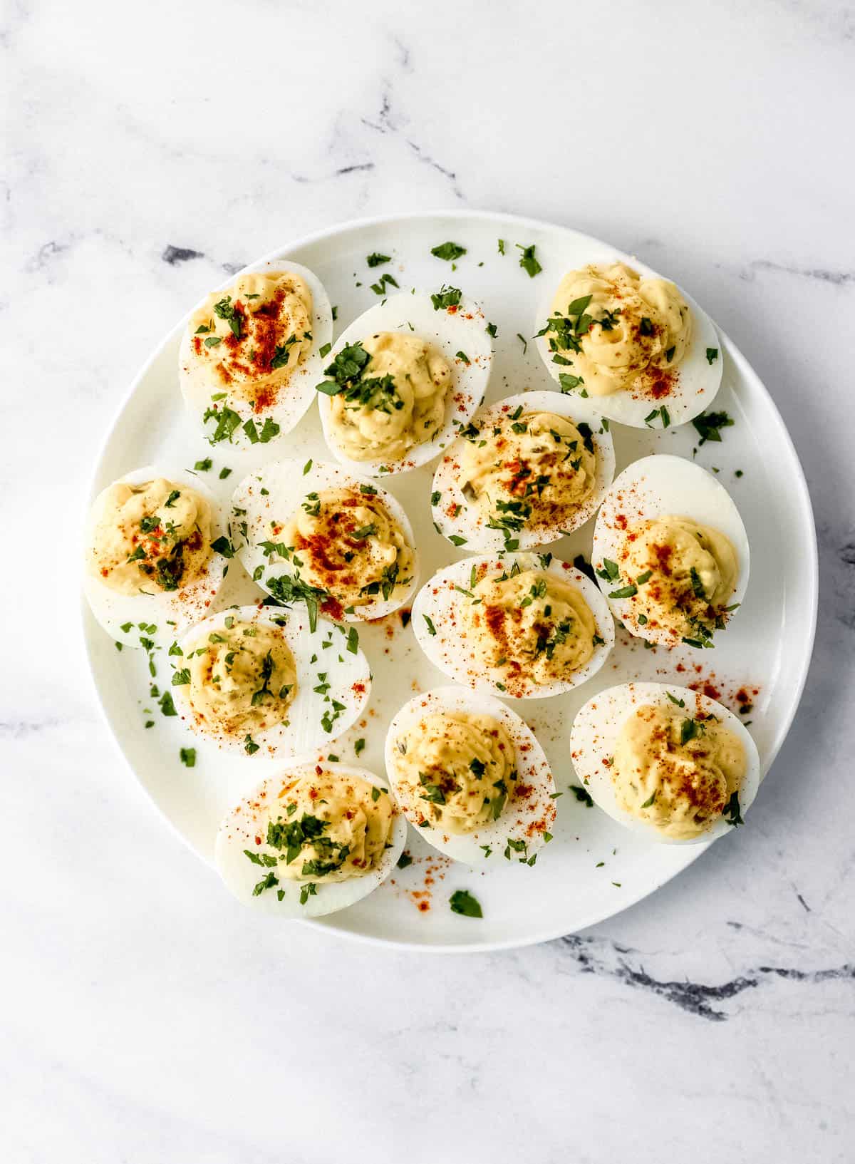 Overhead view of white plate of deviled eggs topped with fresh chopped parsley. 