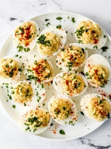 Overhead view of finished deviled eggs on white plate topped with parsley and paprika.