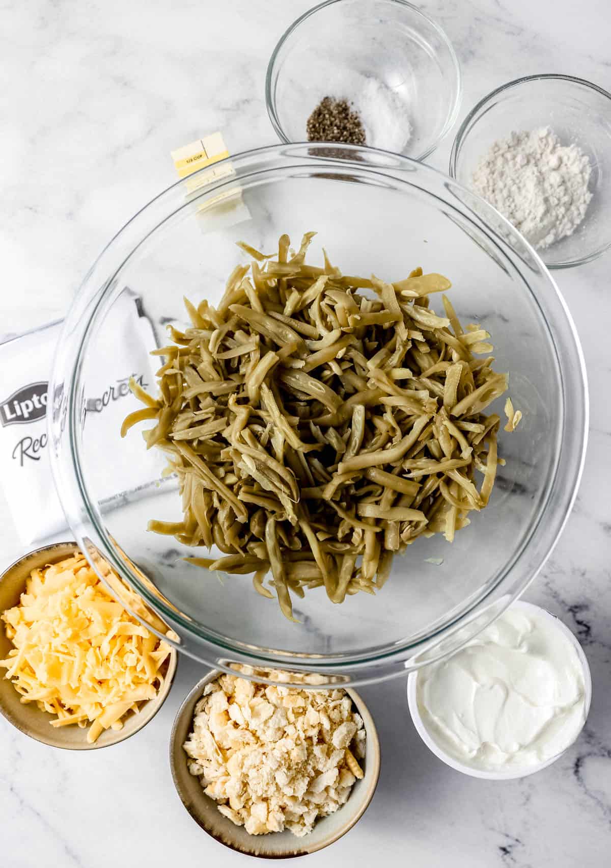 Overhead view of ingredients needed to make casserole in separate containers on marble surface. 