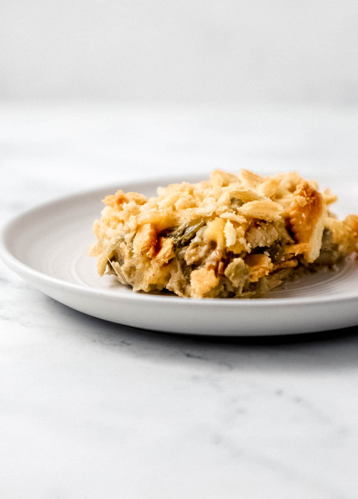 Close up side view of single serving of green bean casserole on white plate. 