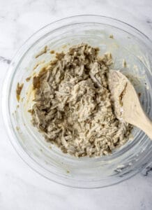 Overhead view of green bean mixture in glass mixing bowl with wooden spoon.