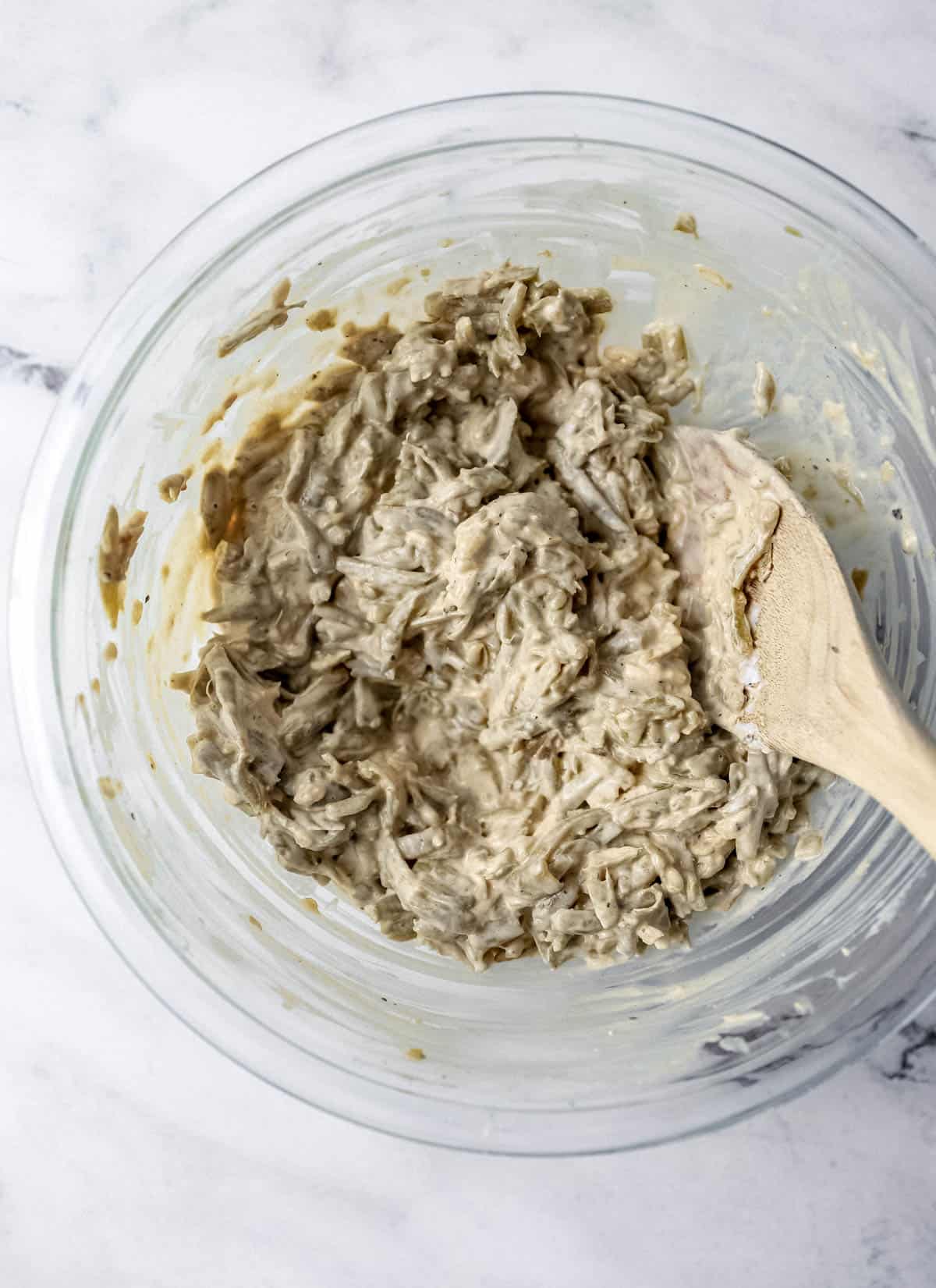 Green bean casserole ingredients combined in glass mixing bowl with wooden spoon. 