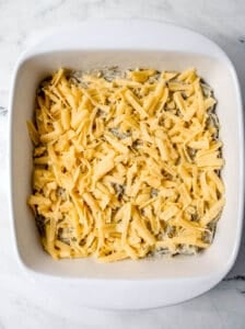 Shredded cheese added to the casserole in a white baking dish.