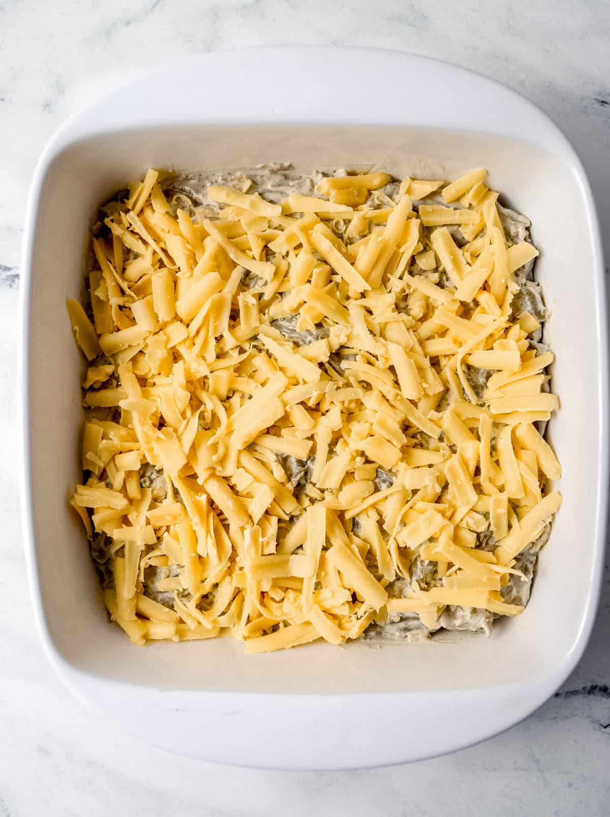 Casserole topped with shredded cheese in square white baking dish. 